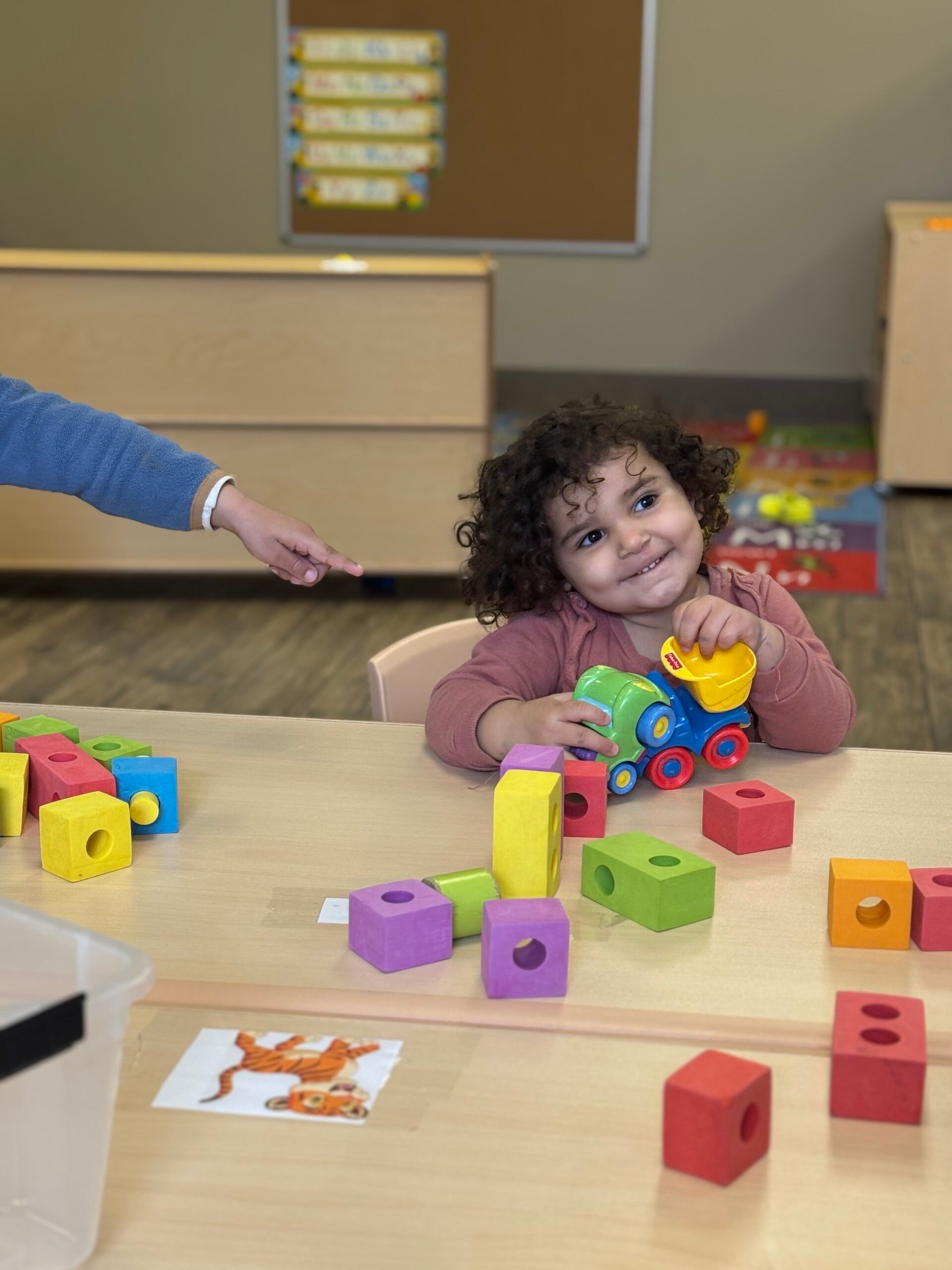 Toddler smiling while playing with colourful blocks and a toy train