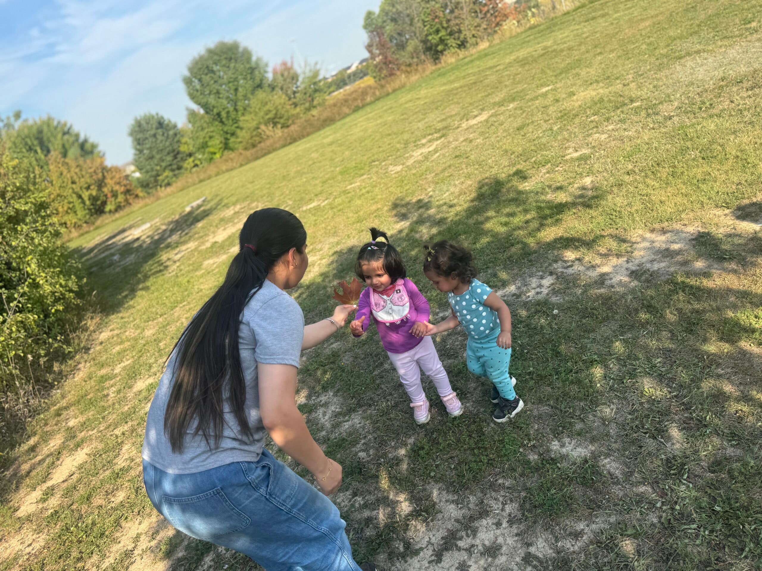Educator playing outdoors with two toddlers on a grassy field